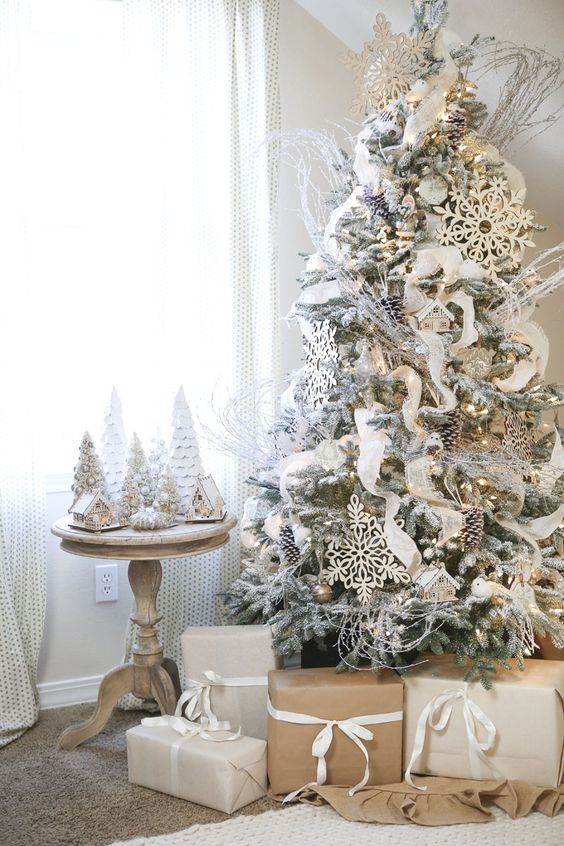 a flocked tree decorated in white and gold, with large snowflakes and snowy pinecones