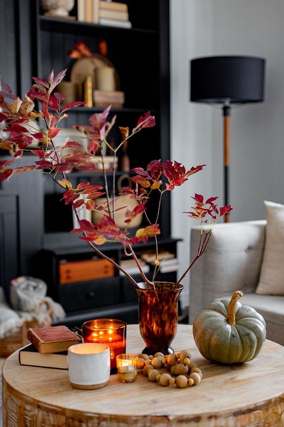 Scandinavian autumn decoration with an amber vase and bold leaves, a pumpkin, beads, books and candles
