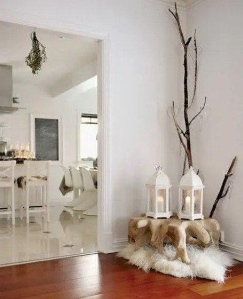 a Nordic decoration made of a wooden table, a faux fur rug, branches and white candle lanterns