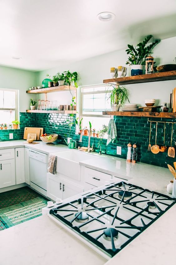 a boho kitchen with white cabinets, a bright green tile backsplash, lots of greenery and green rugs