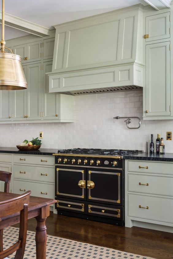 a bright art deco kitchen in pale green, with a white tile backsplash, a vintage cooker and gold touches