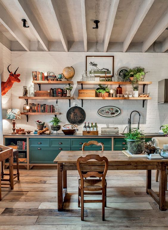 a bright eclectic kitchen pairing teal cabinets, rustic wooden furniture, potted plants and a faux animal head