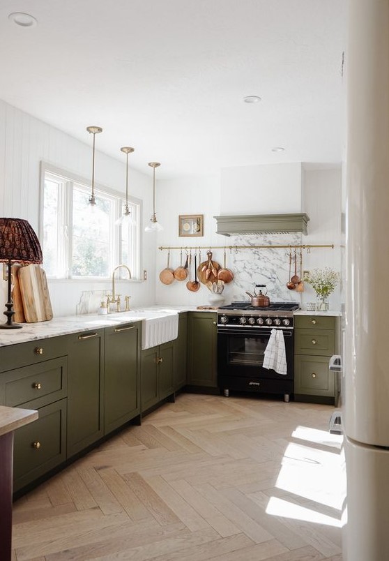a chic kitchen with a row of green cabinets, white marble countertops and pendant lamps, a built-in hood and some lamps