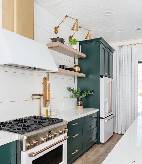 a chic kitchen with forest green and white cabinets, open shelves, gold and brass fixtures and some greenery