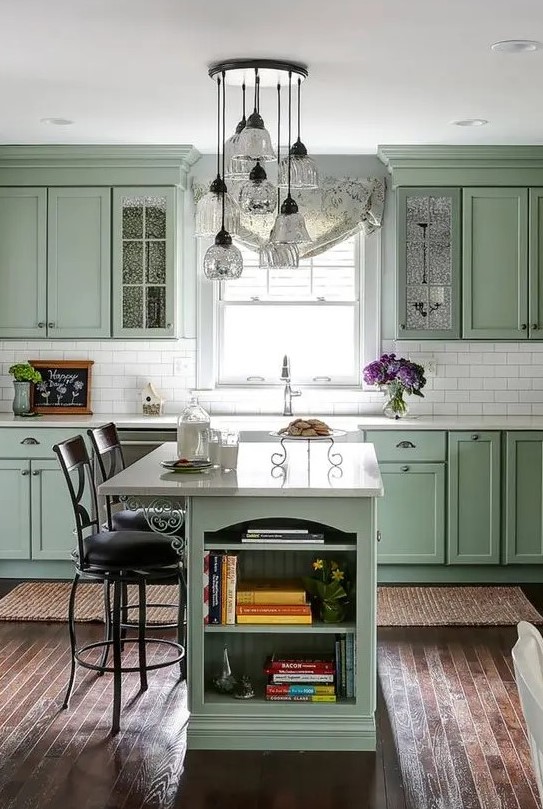 a chic vintage sage green kitchen with elegant cabinetry, a white tile backsplash and countertops, a small kitchen island with storage