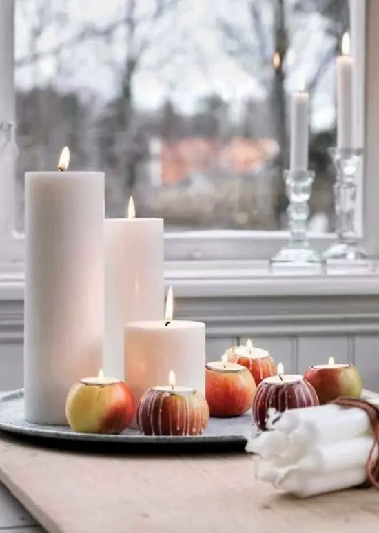 An autumnal Nordic centerpiece consisting of a tray of pillar candles and apples with candles in them is a very simple decoration