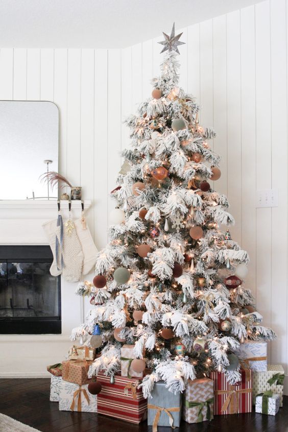 a flocked Christmas tree styled with green and beige ornaments, lights and bells is a cool and catchy decoration