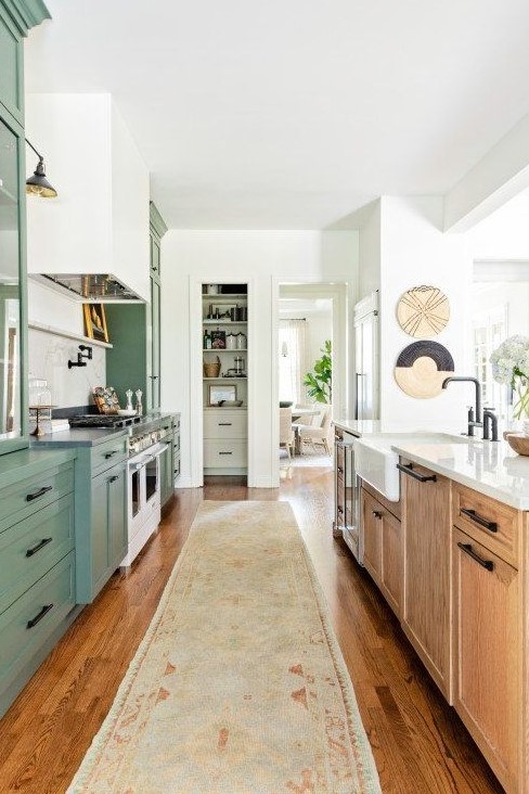 a kitchen with green and stained cabinets, a white tile backsplash, black handles and some lovely decor