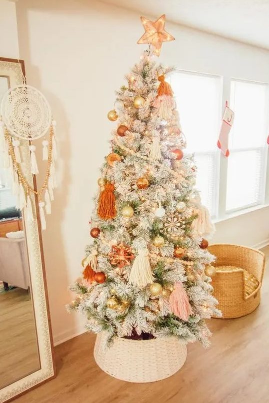 a lovely flocked Christmas tree with pastel boho decor, orange, gold and blush ornaments, beadsm large tassels and lights