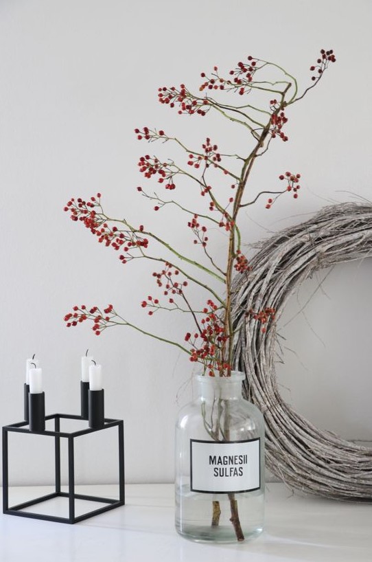 a matte black candelabra with candles, branches with berries in a glass bottle and a whitewashed grapevine wreath