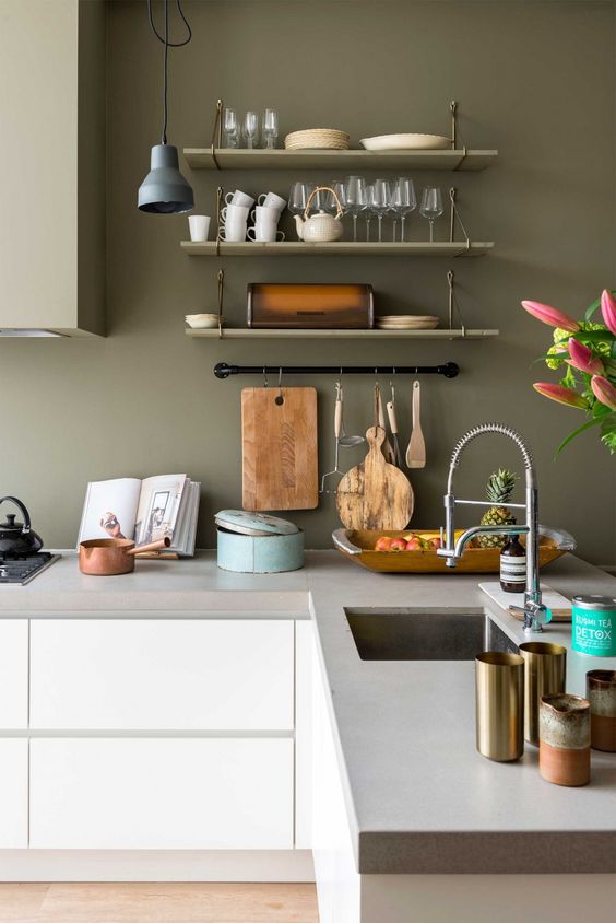 a minimalist kitchen with olive green walls and a hood, sleek white cabinets with a concrete countertop and pendant lamps