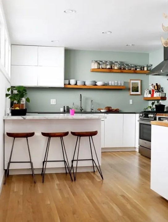 a minimalist kitchen with white cabinets, sage green walls, stone countertops and wooden shelves and stools