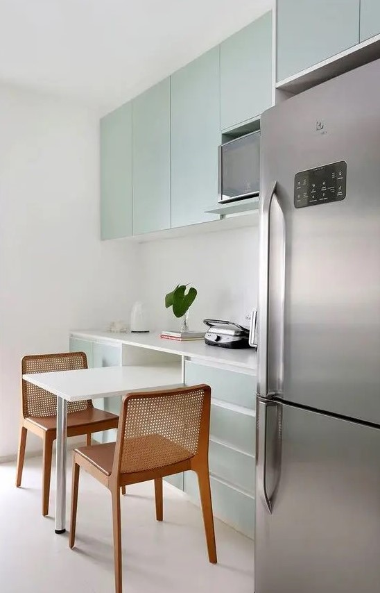 a minimalist mint flat panel kitchen with a white stone backsplash and countertops and stainless steel touches