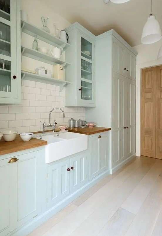 a mint green kitchen with shaker cabinets, a stained countertop, a white subway tile backsplash plus brass handles