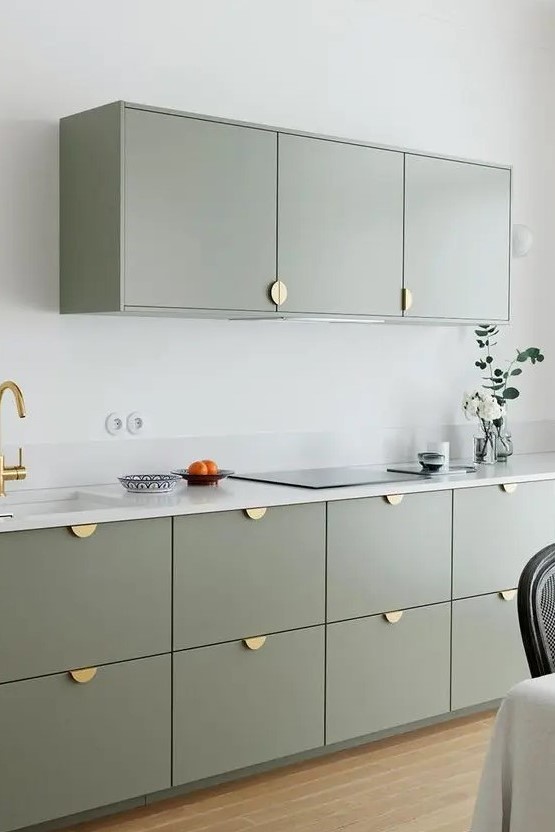a modern and laconic kitchen with sage green cabinets, gold pulls, a white stone countertop and a small backsplash is chic