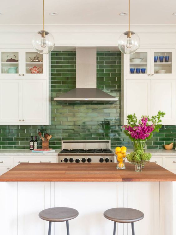 a modern white kitchen with shaker cabinets, a green tile backsplash, a kitchen island with a butcherblock countertop and pendant lamps