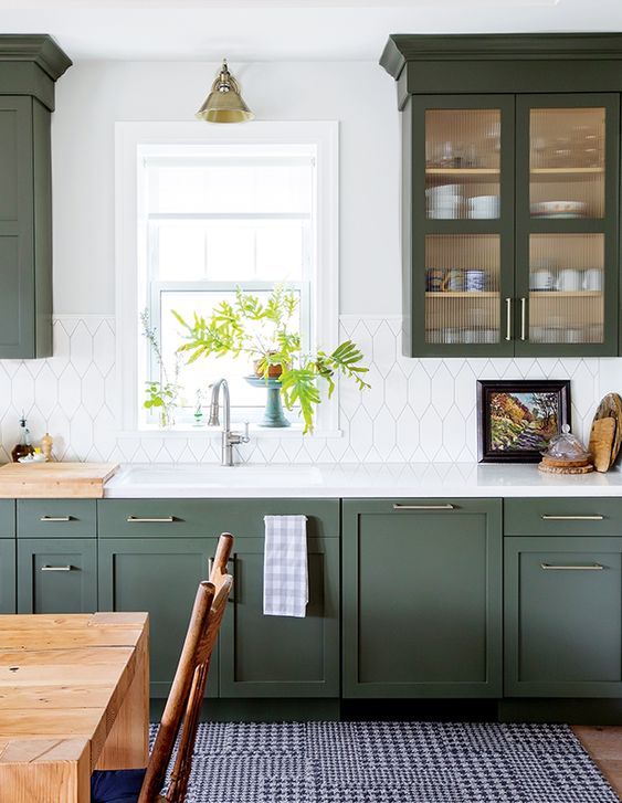 a refined green kitchen with shaker style cabinets, a white stone backsplash and countertops and some touches of wood