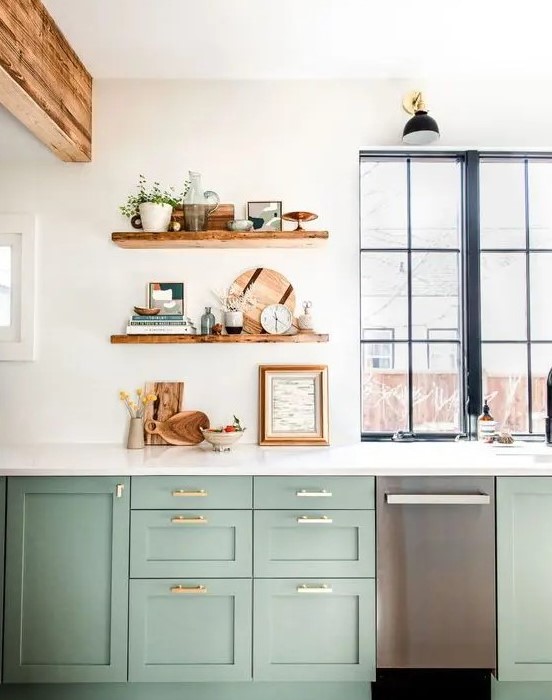 a sage green farmhouse kitchen with shaker cabinets, open shelves, white stone countertops, wooden beams and black framed windows