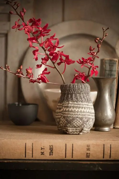 A vase wrapped with a piece of knitting and branches with burgundy flowers looks laconic and cozy