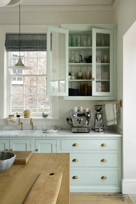 a vintage pastel green kitchen with a white stone countertops, glass door cabinets, vintage pendant lamps