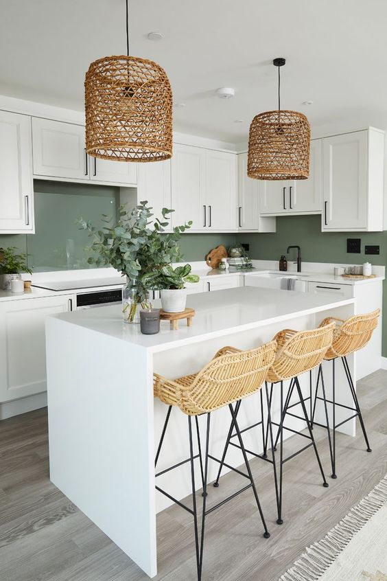 a white farmhouse kitchen with shaker cabinets and a kitchen island, a green backsplash and woven pendant lamps
