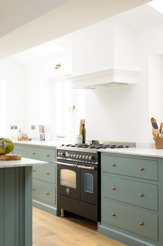 an elegant kitchen with white walls and green cabinets, a matching kitchen island, a white hood and a black cooker