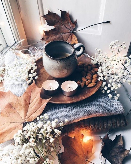 Cozy and simple Nordic autumn decoration with a pile of blankets, gypsophila and leaves, candles, nuts and coffee