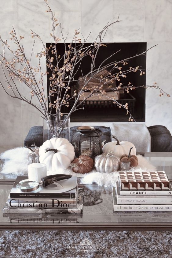 Elegant Scandinavian autumn decoration with dried branches in a vase, a candle lantern and some pumpkins on the faux fur