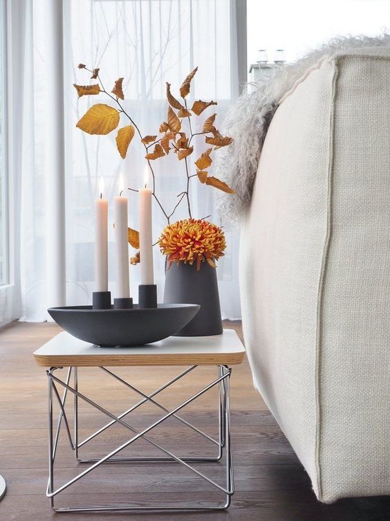 A Scandinavian autumn decoration with a black vase with flowers and autumn leaves and candles in a candle holder is a nice idea