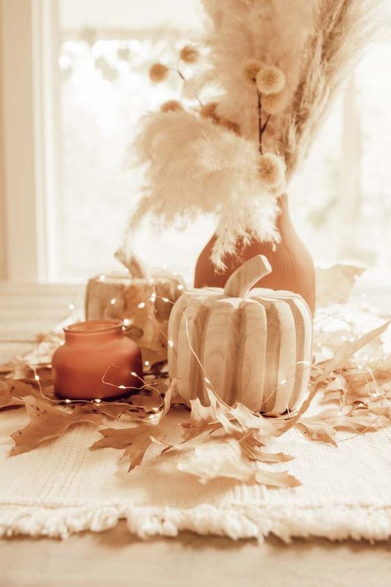 Neutral autumn decoration with wooden pumpkins, a glass with a candle, a wooden vase with dried grasses, lights and leaves
