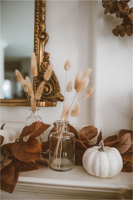Simple Scandinavian fall decor with leaves, grasses in clear vases and white pumpkins is a cool and chic idea