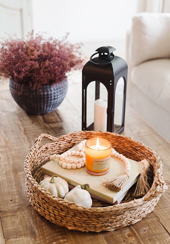Stylish Scandinavian autumn decoration with a basket, pumpkins, books, wooden beads, a candle, a candle lantern and some pink flowers in a planter