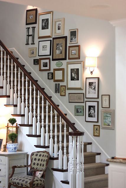 an eclectic gallery wall in the stairwell with mismatched frames and artwork, photos and monograms and a sconce to highlight them