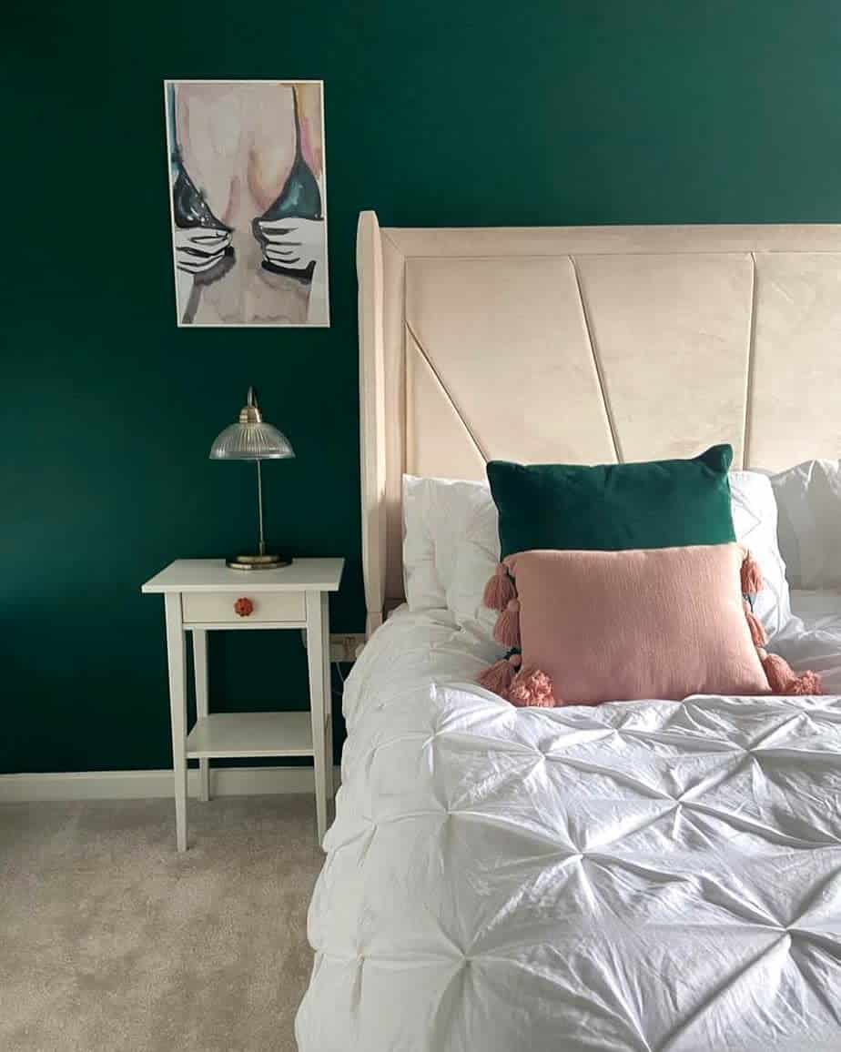 Dark green accent wall, cream headrest, platform, bed, white nightstand, woman undressing, wall art