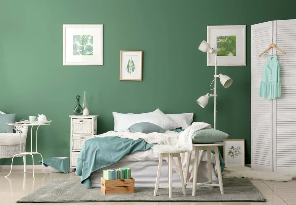Large green bedroom, white bedside table, chair and shelf lamp, framed leaf paintings 
