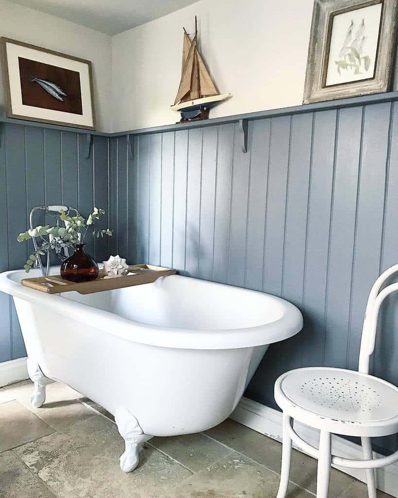 Blue wall paneling in the bathroom, white bathtub and vintage chair 