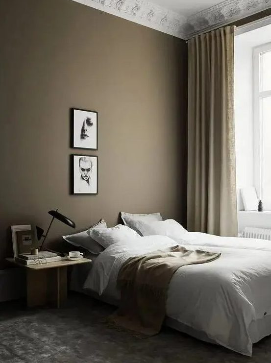 A beautiful Scandinavian bedroom with a taupe accent wall, bed, light stained nightstand, small gallery wall and brown and gold accents