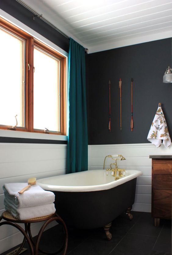 a beautiful bathroom with sooty walls, white tiles, a black freestanding bathtub, a stool, a stained vanity and teal curtains