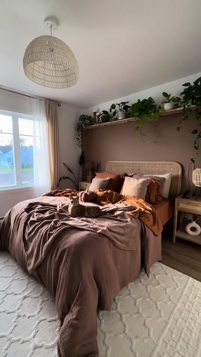 A beautiful, earthy bedroom with a chocolate brown accent wall, a bed with a cane headboard, rust and chocolate bedding, and cane nightstands