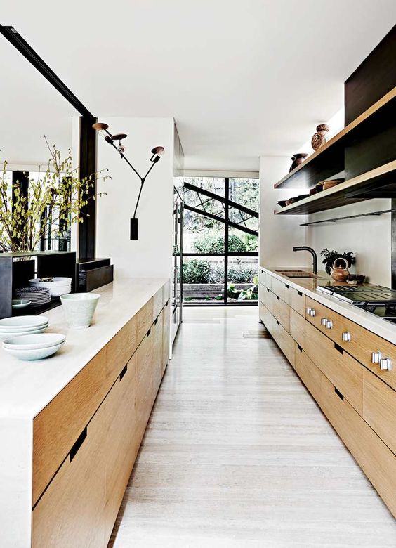 A beautiful, modern, narrow kitchen with stained cabinets, open shelving, white countertops, sconces and various decor
