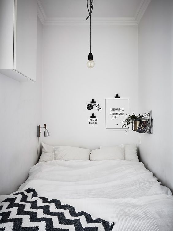 A black and white narrow Scandinavian bedroom with a squeezed in bed, a shelf, some decor and black and white bedding
