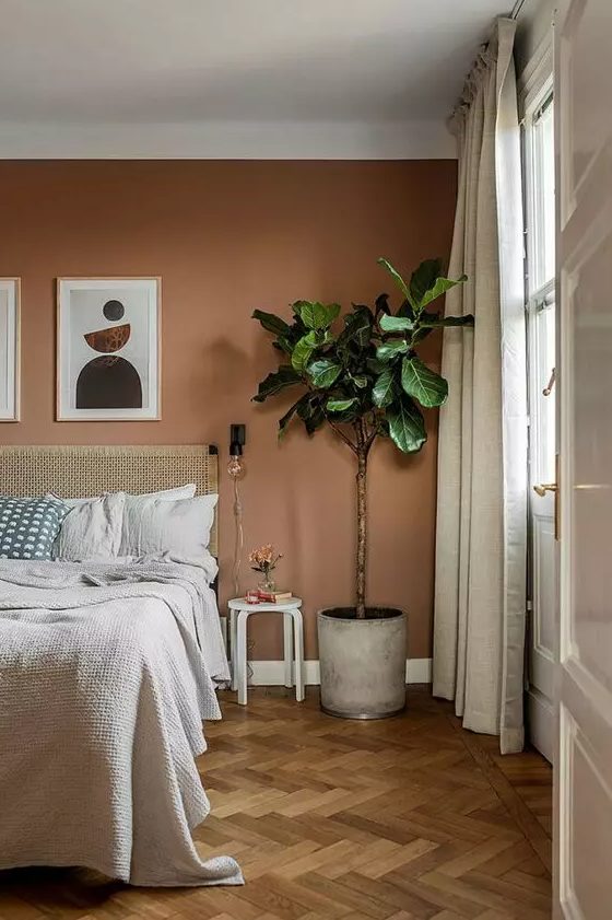 a boho bedroom with a terracotta accent wall, a bed with woven linens, a potted plant and a stool as a side table