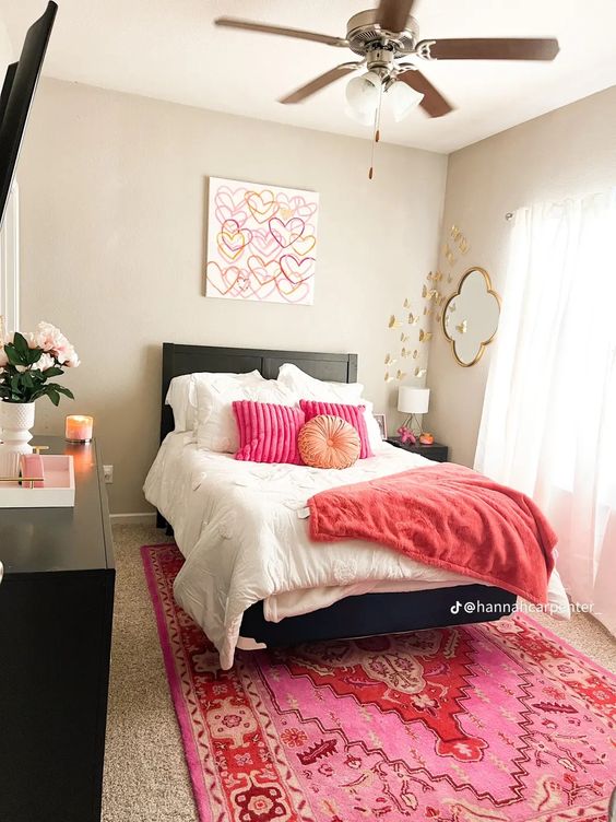 A bright and cool modern teenage girl's room with black furniture, pink textiles, an artwork, gold butterflies and a mirror and some flowers