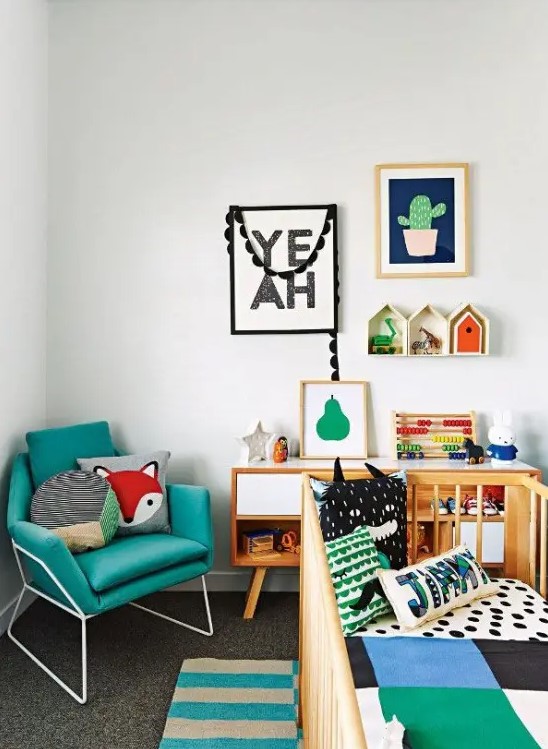 A bright, mid-century modern nursery with a turquoise chair, a crib with bright linens, a statement rug, and a colorful gallery wall