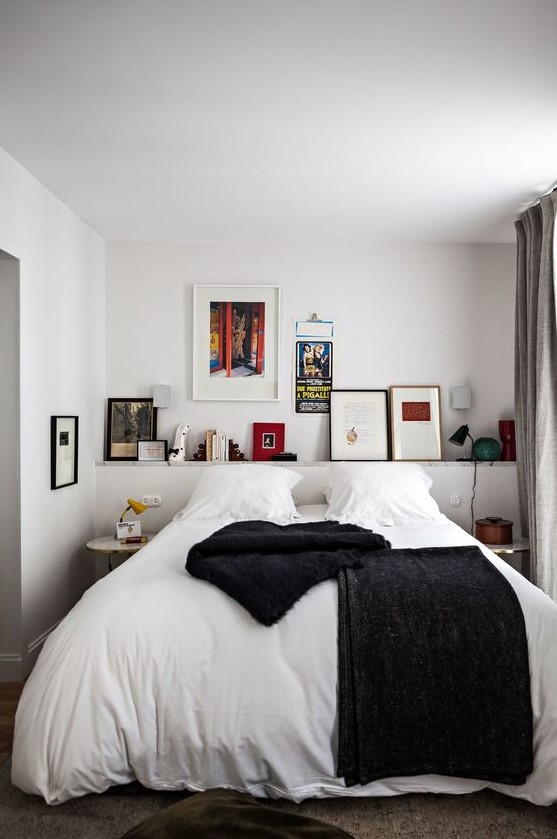 a striking and contrasting bedroom with a bar of artwork and books, a bed with contrasting linens, bedside tables and a black lamp