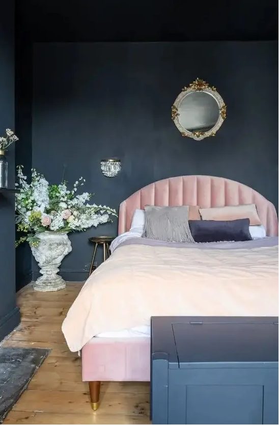 a chic, atmospheric bedroom with soot walls and a chest for storage, a light pink bed, sophisticated lighting and flowers