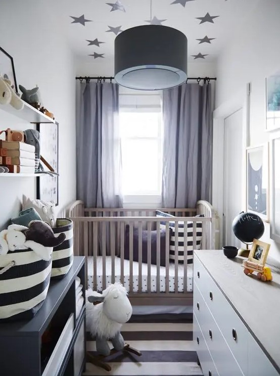 a chic little nursery with a stained cot, a white and a black dresser, a striped rug and printed bedding, a wall shelf and toys