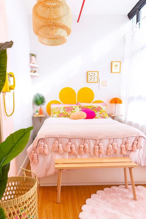 A colorful, modern teen room with a bed and pink and yellow linens, a bench, a basket and artwork