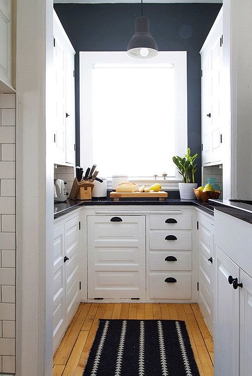 A contrasting U-shaped kitchen with white cabinets, dark blue walls, black fixtures, and black countertops is super chic