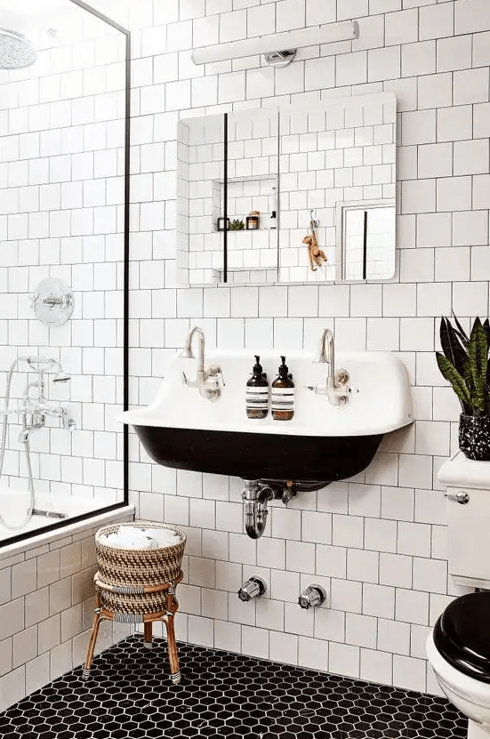 a contrasting modern bathroom with white square tiles and hexagonal tiles on the floor, a black wall-mounted sink, a mirror and some potted plants
